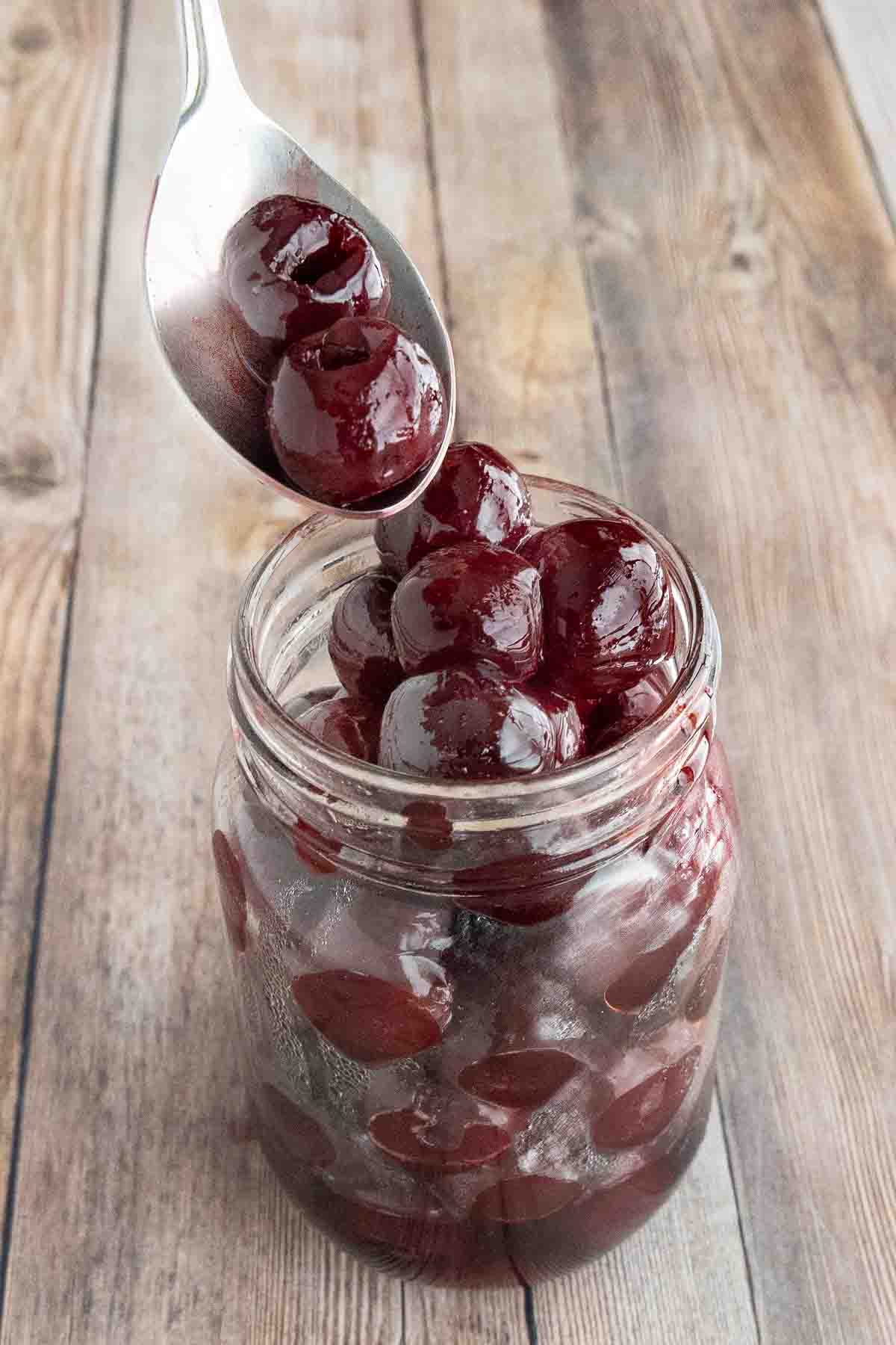 A spoon coming out of a jar of maraschino cherries.