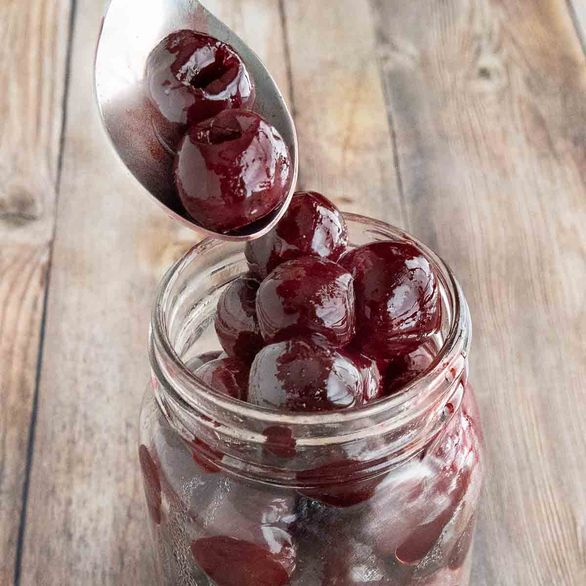 A spoon coming out of a jar of maraschino cherries.