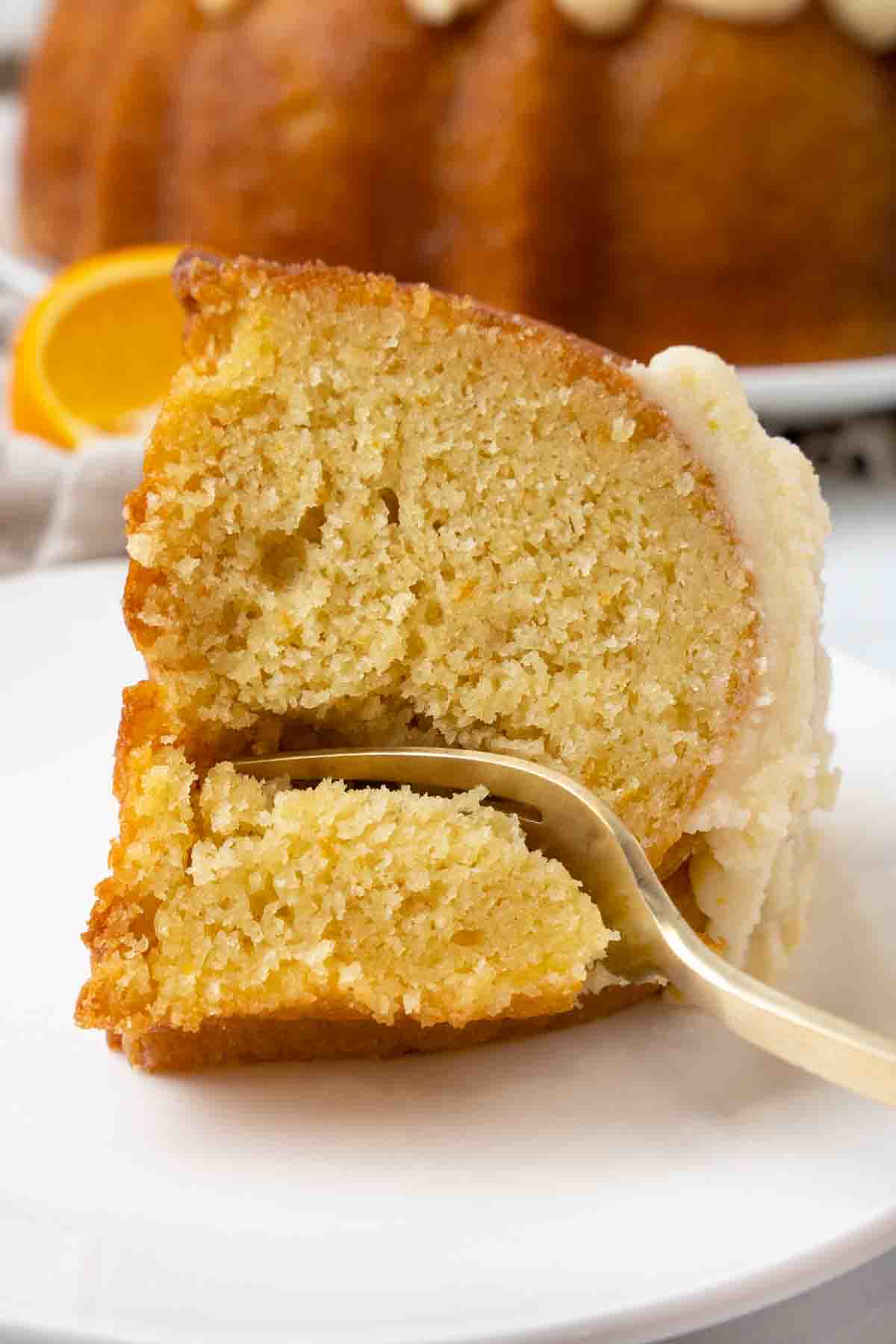 Slice of orange cake with a fork in it on a white plate.