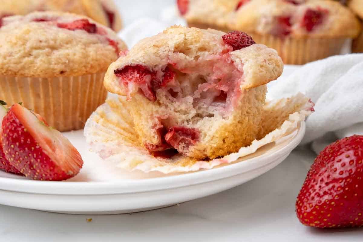 Strawberry muffin with a bite out of it with muffin paper pulled off the sides