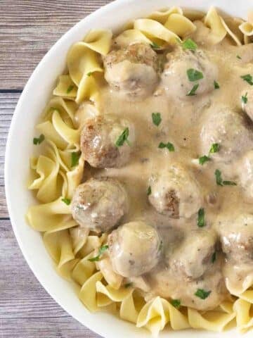 Swedish meatballs over egg noodles in a white bowl.