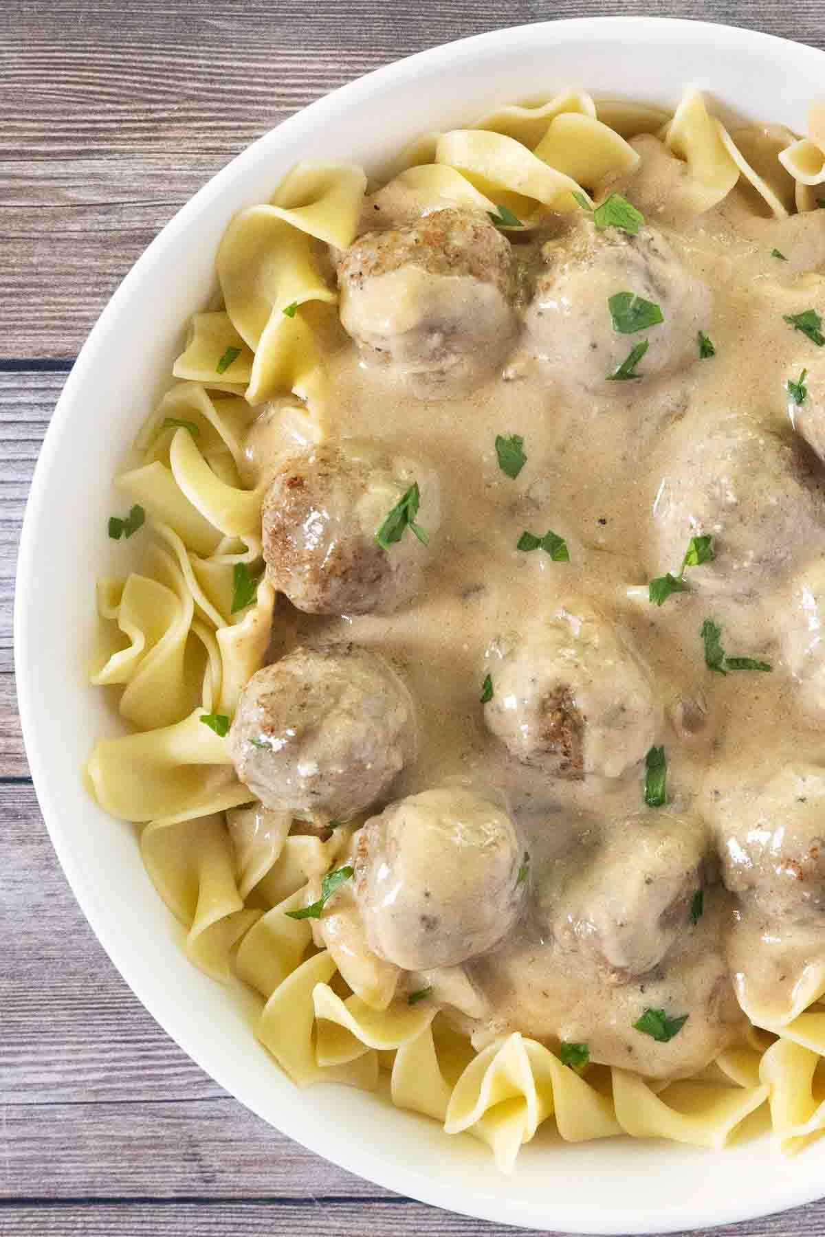 Swedish meatballs over egg noodles in a white bowl.
