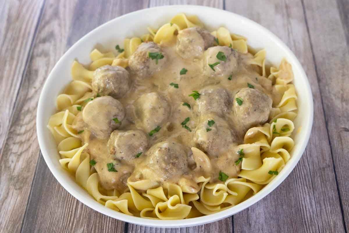 Swedish meatballs over egg noodles in a white bowl.