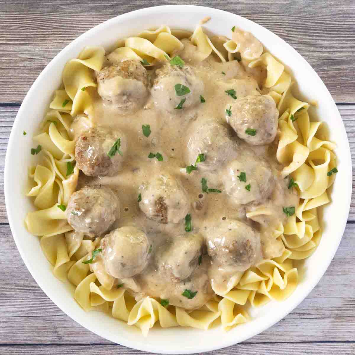 Swedish meatballs over egg noodles in a white bowl.