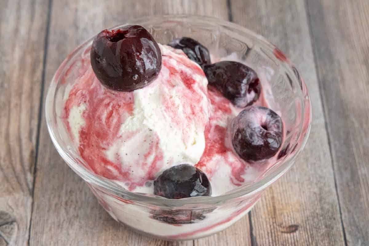 maraschino cherries over ice cream in a glass bowl.