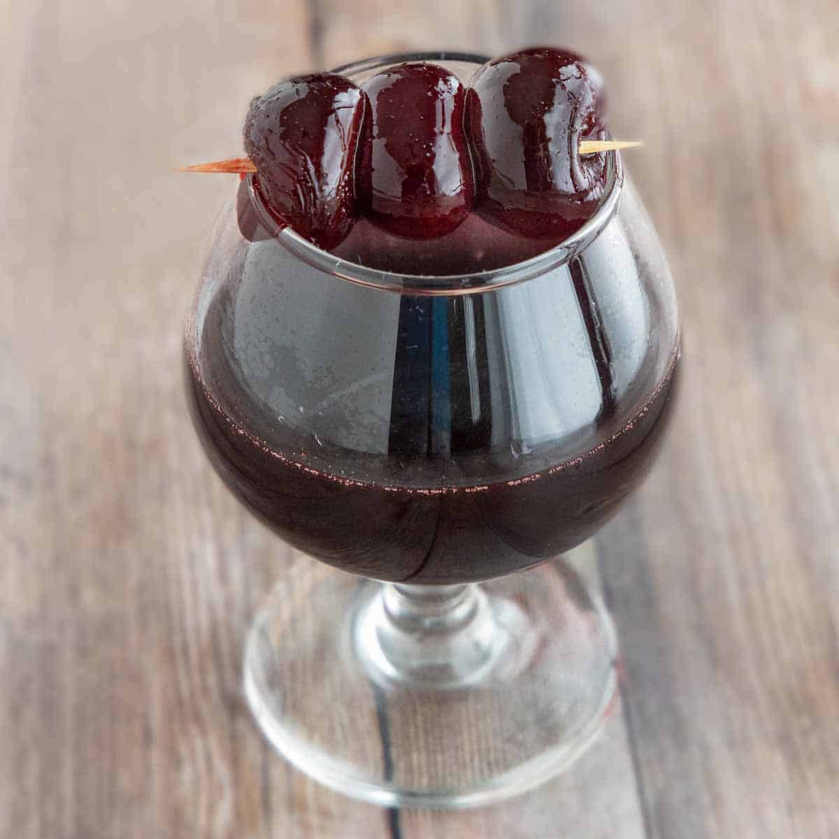 maraschino cherries on a toothpick over a glass of cherry liquour.