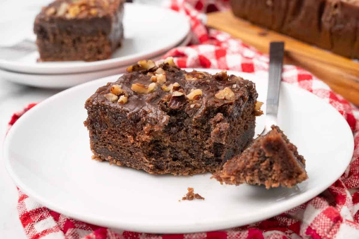 Slice of coca cola cake on a white plate with a fork taking a piece out.
