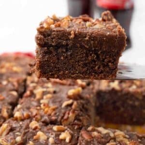 Slice of coca cola cake being taken out of the whole cake.