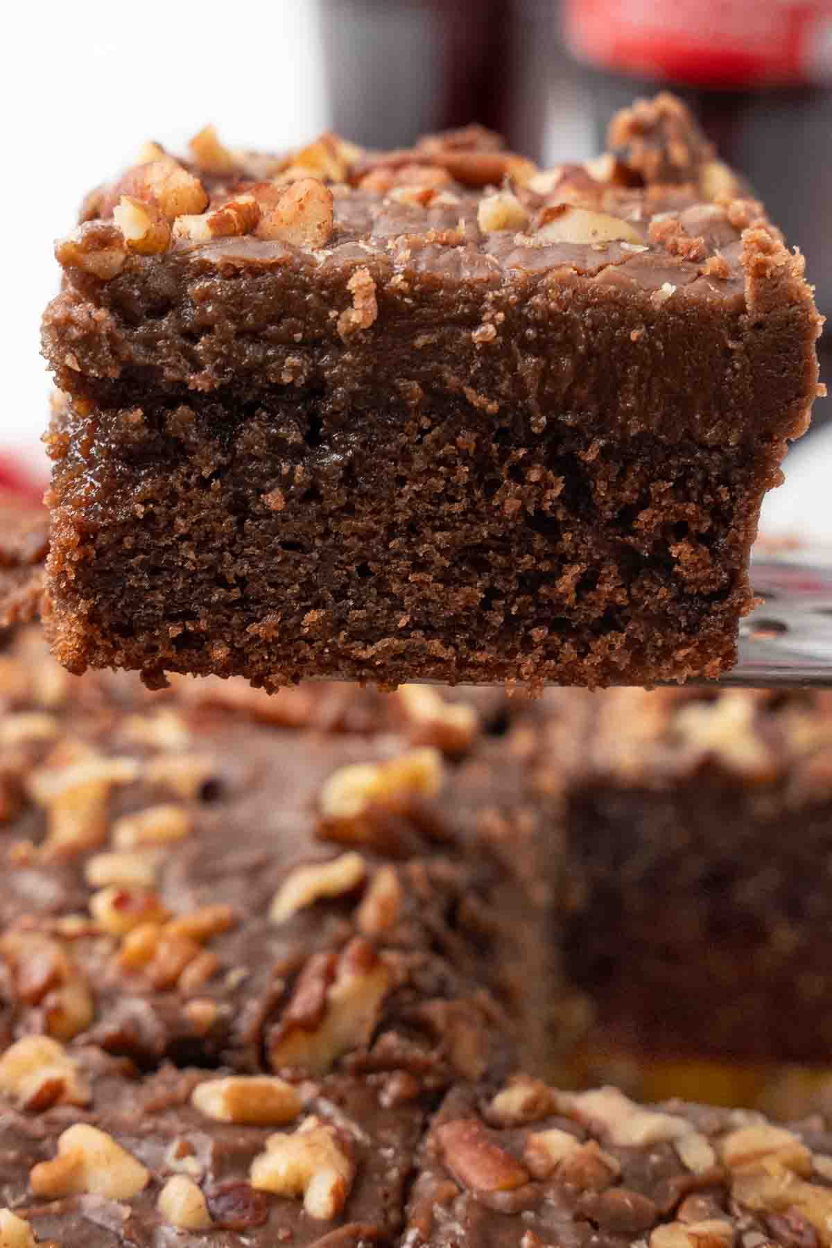 Slice of coca cola cake being taken out of the whole cake.
