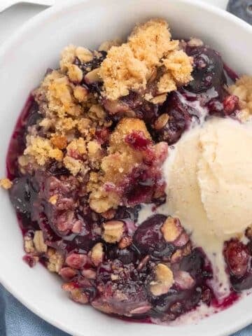 blueberry crisp with vanilla ice cream in a white bowl.
