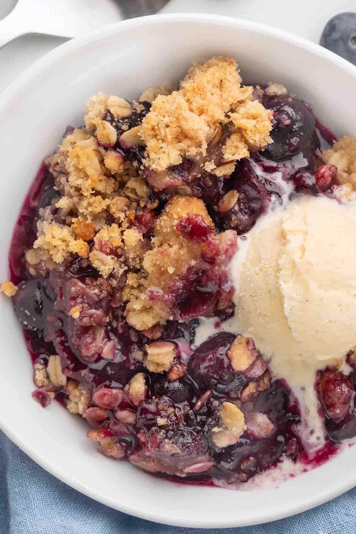 blueberry crumble with vanilla ice cream in a white bowl.