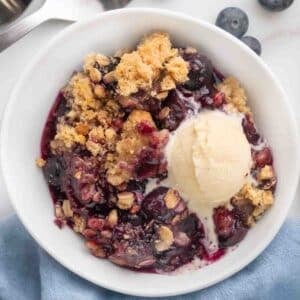 blueberry crumble with vanilla ice cream in a white bowl.