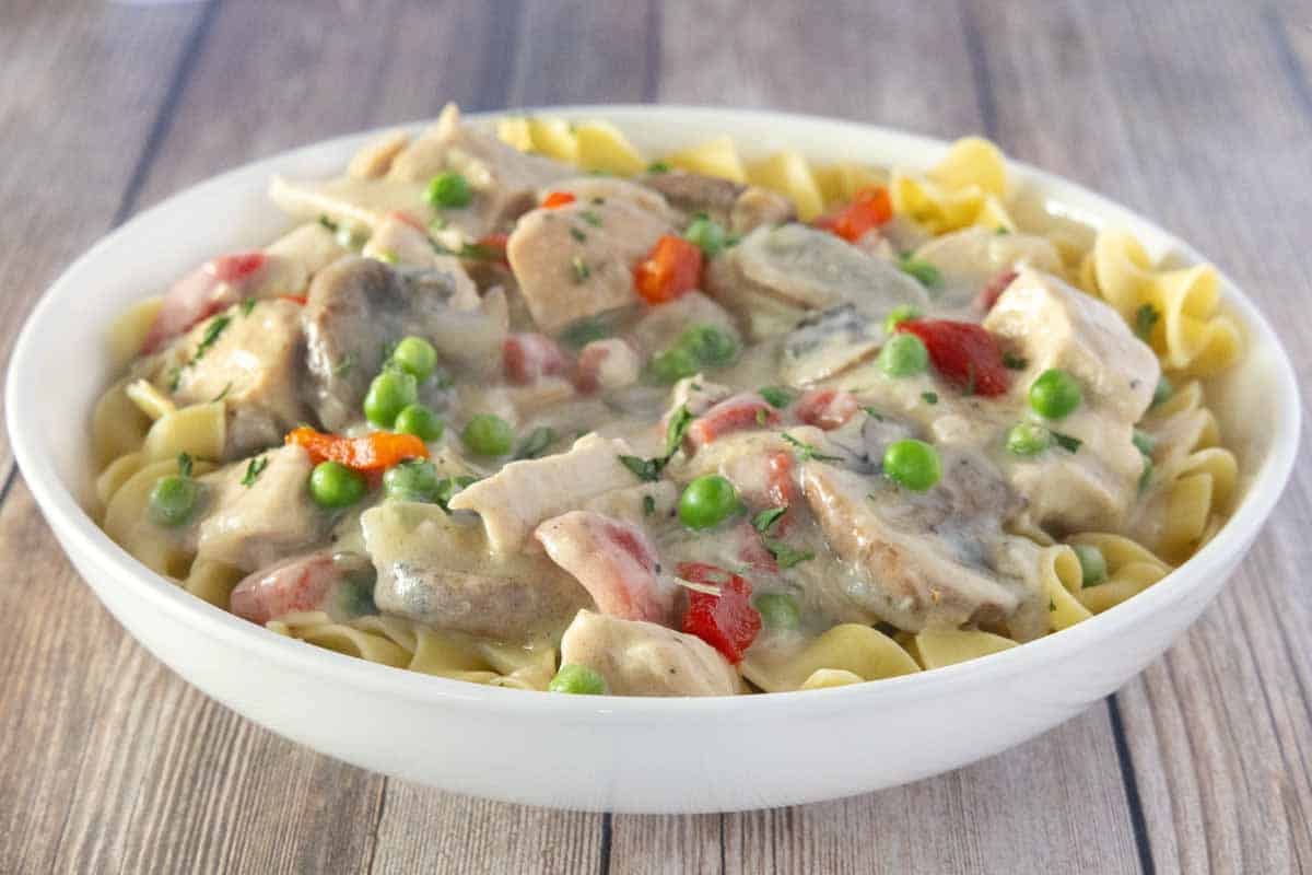 Chicken a la king over egg noodles in a white bowl.