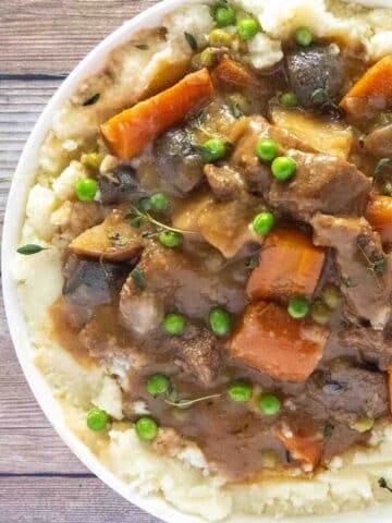 Crockpot beef stew over mashed potatoes in a white bowl.