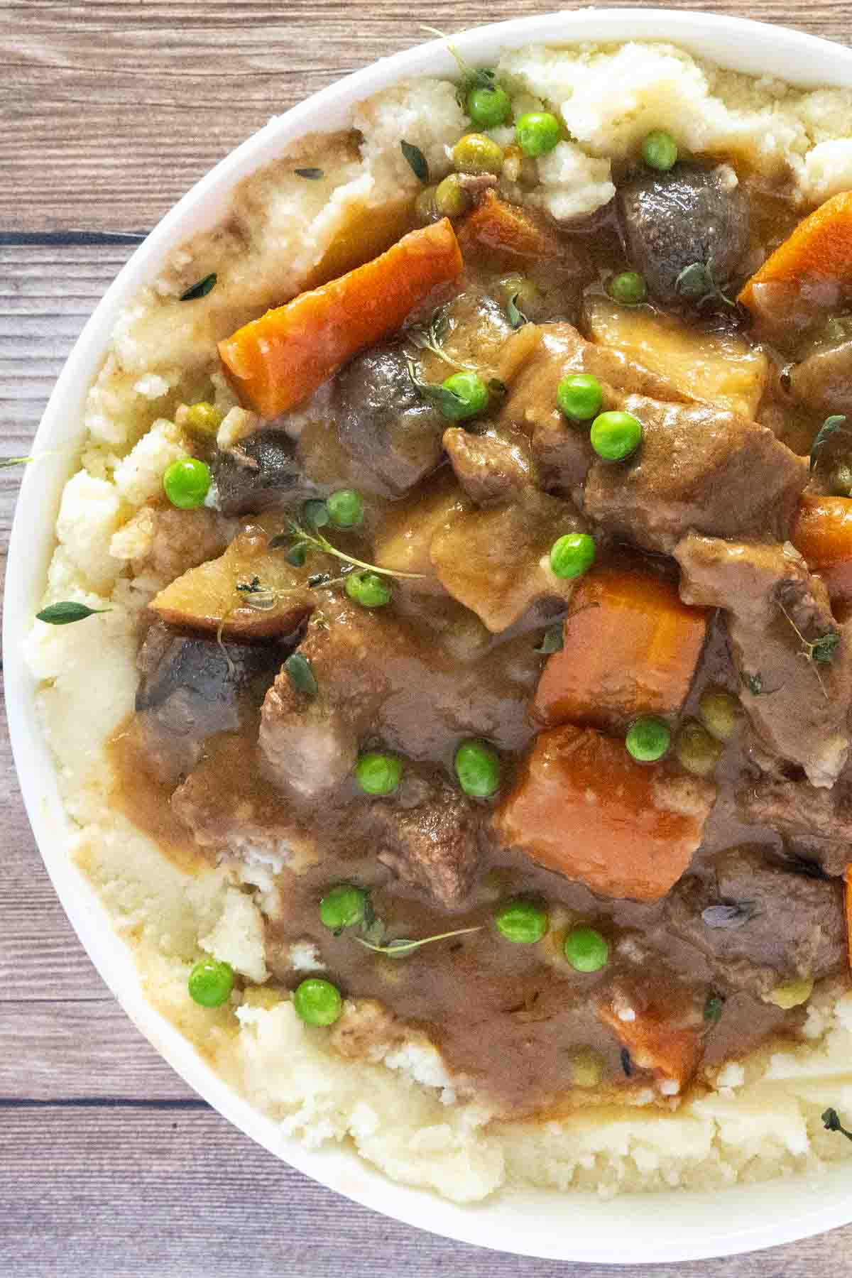 Crockpot beef stew over mashed potatoes in a white bowl.