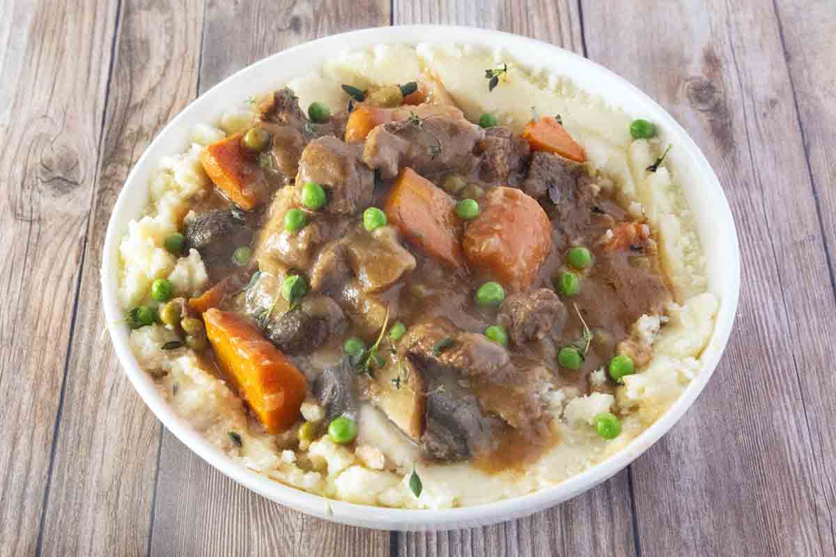 Crockpot beef stew over mashed potatoes in a white bowl.