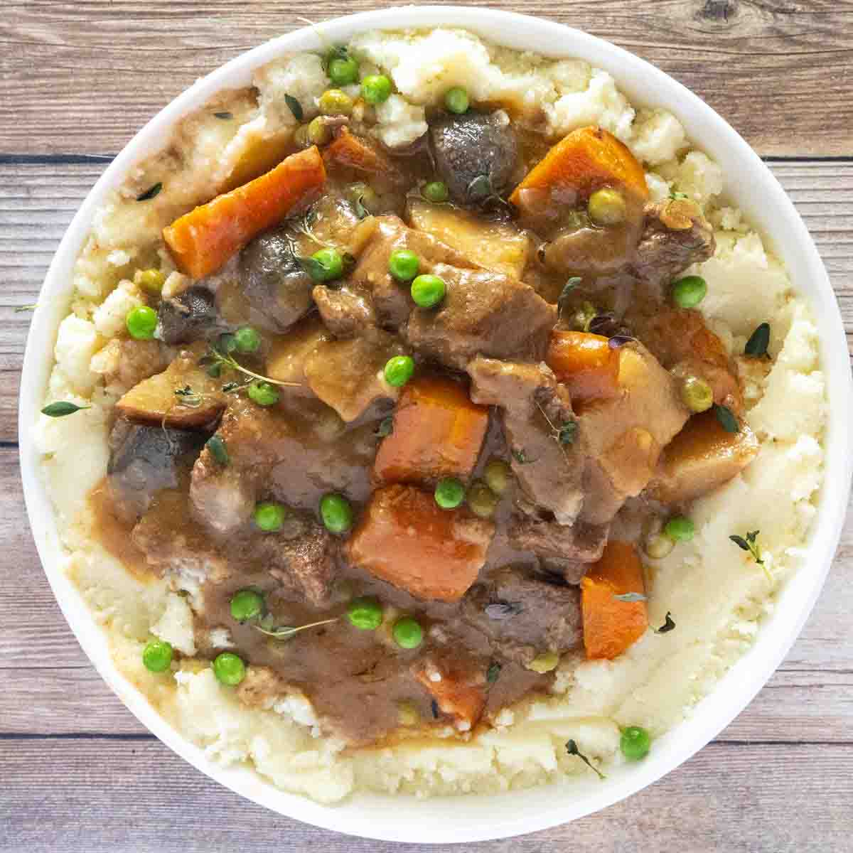 Crockpot beef stew over mashed potatoes in a white bowl.