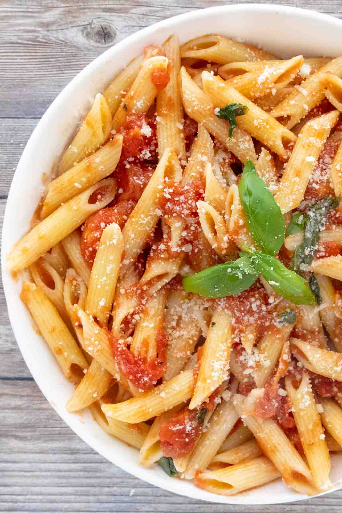 Pasta pomodoro in a white bowl with a sprig of basil in the middle.