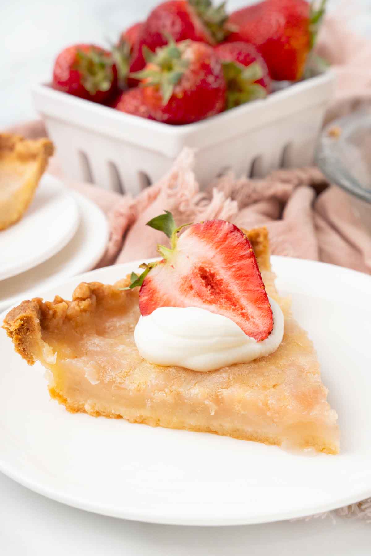 Slice of water pie topped with whipped cream and a strawberry on a white plate.