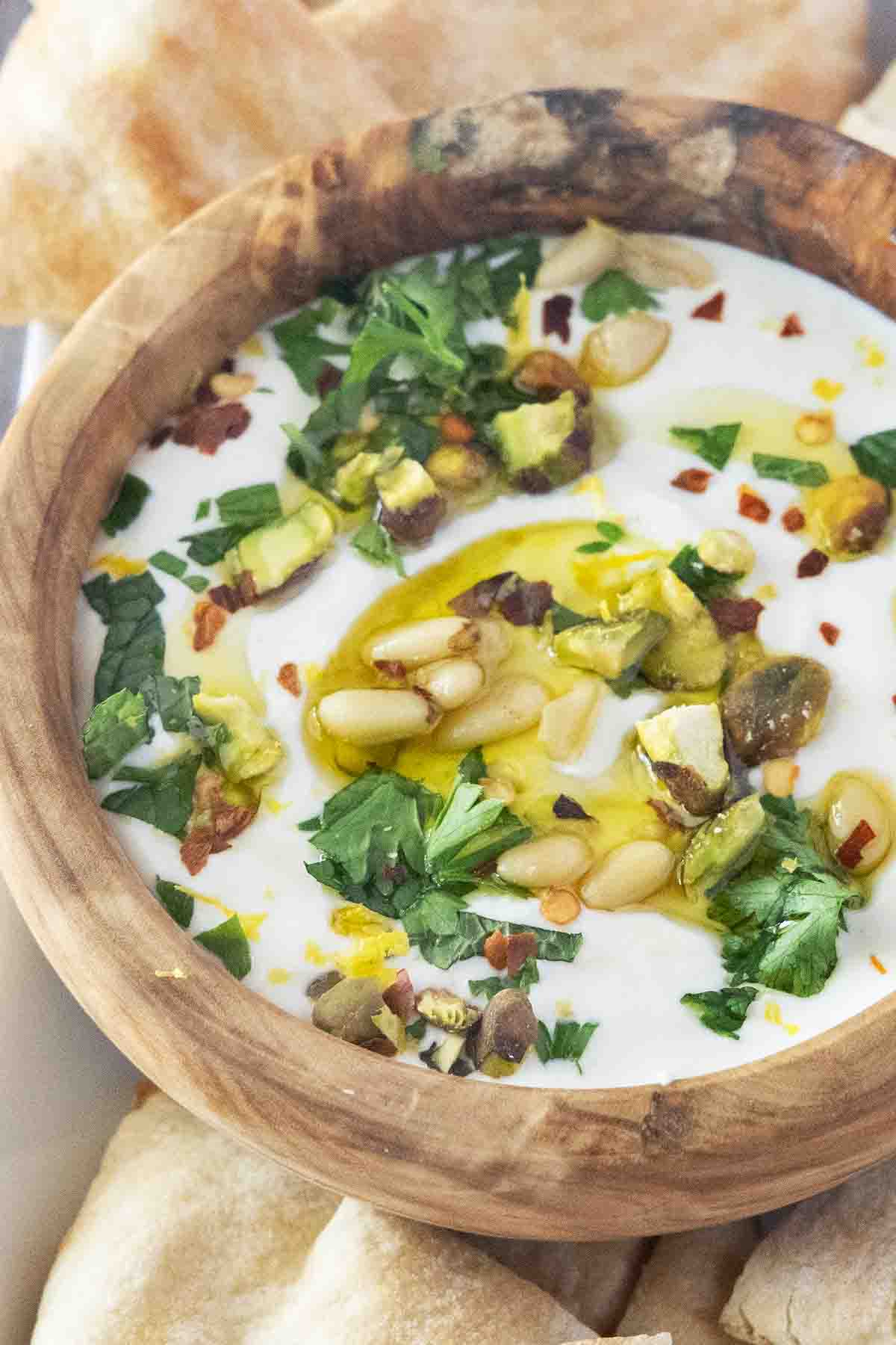 Whipped feta cheese dip in a wooden bowl with pita chips on a white platter.