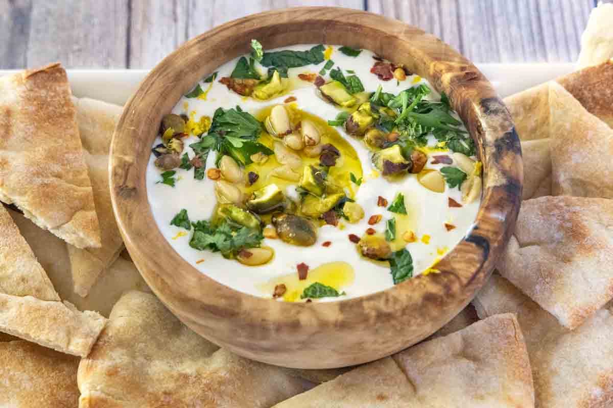 Whipped feta cheese dip in a wooden bowl with pita chips on a white platter 