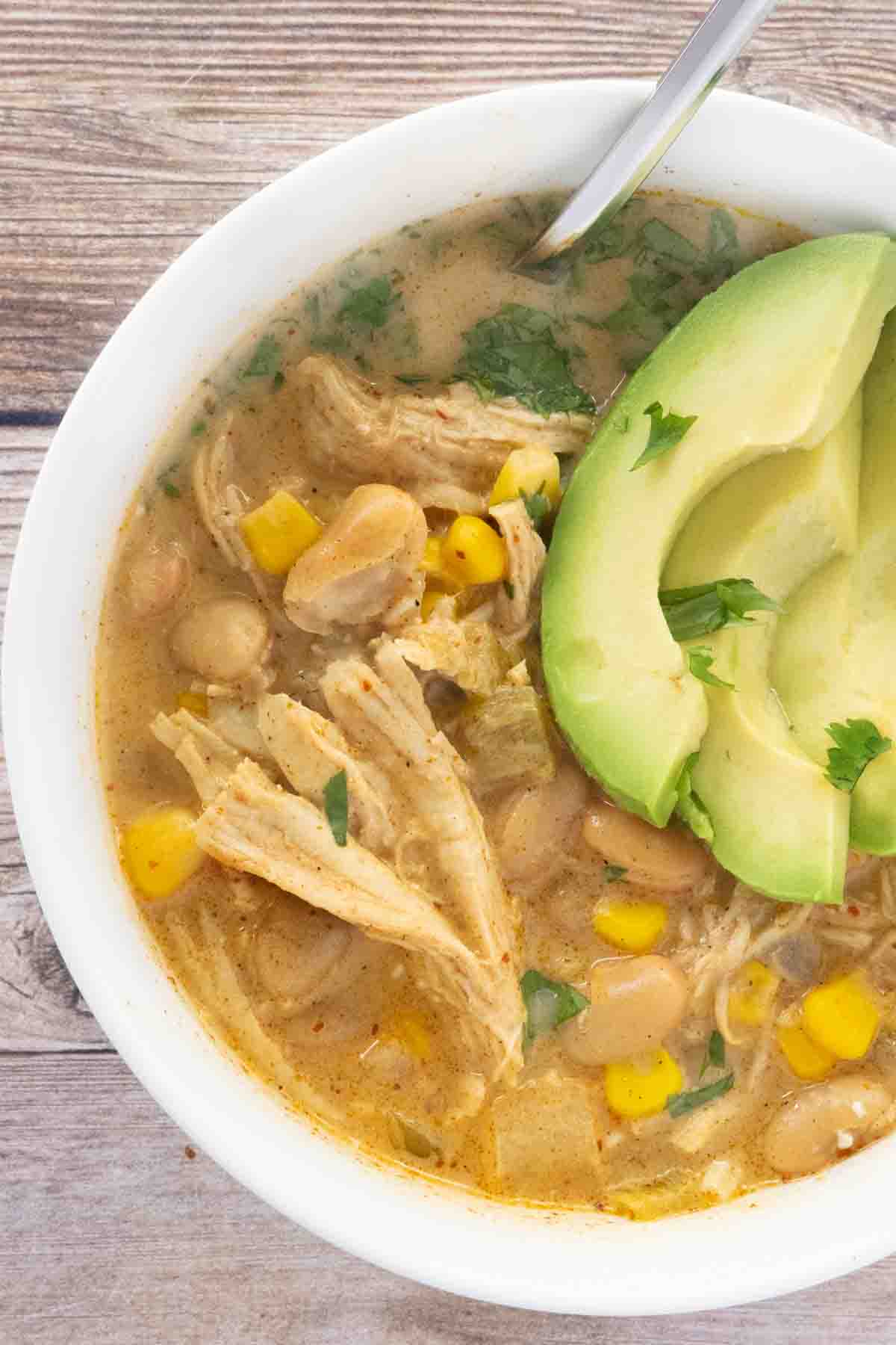 White bean chicken chili with sliced avocado in a white bowl.