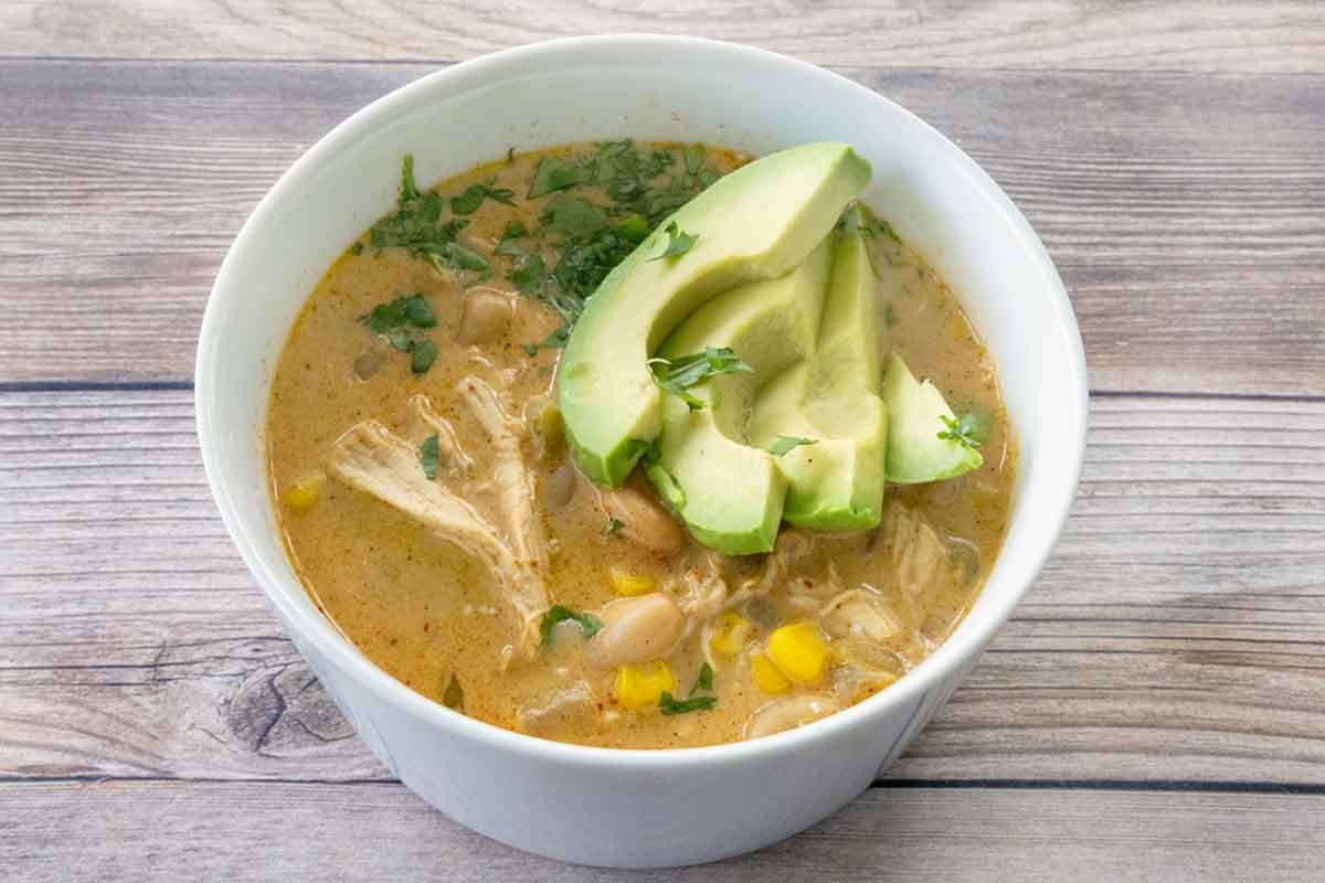 White bean chicken chili with sliced avocado in a white bowl.