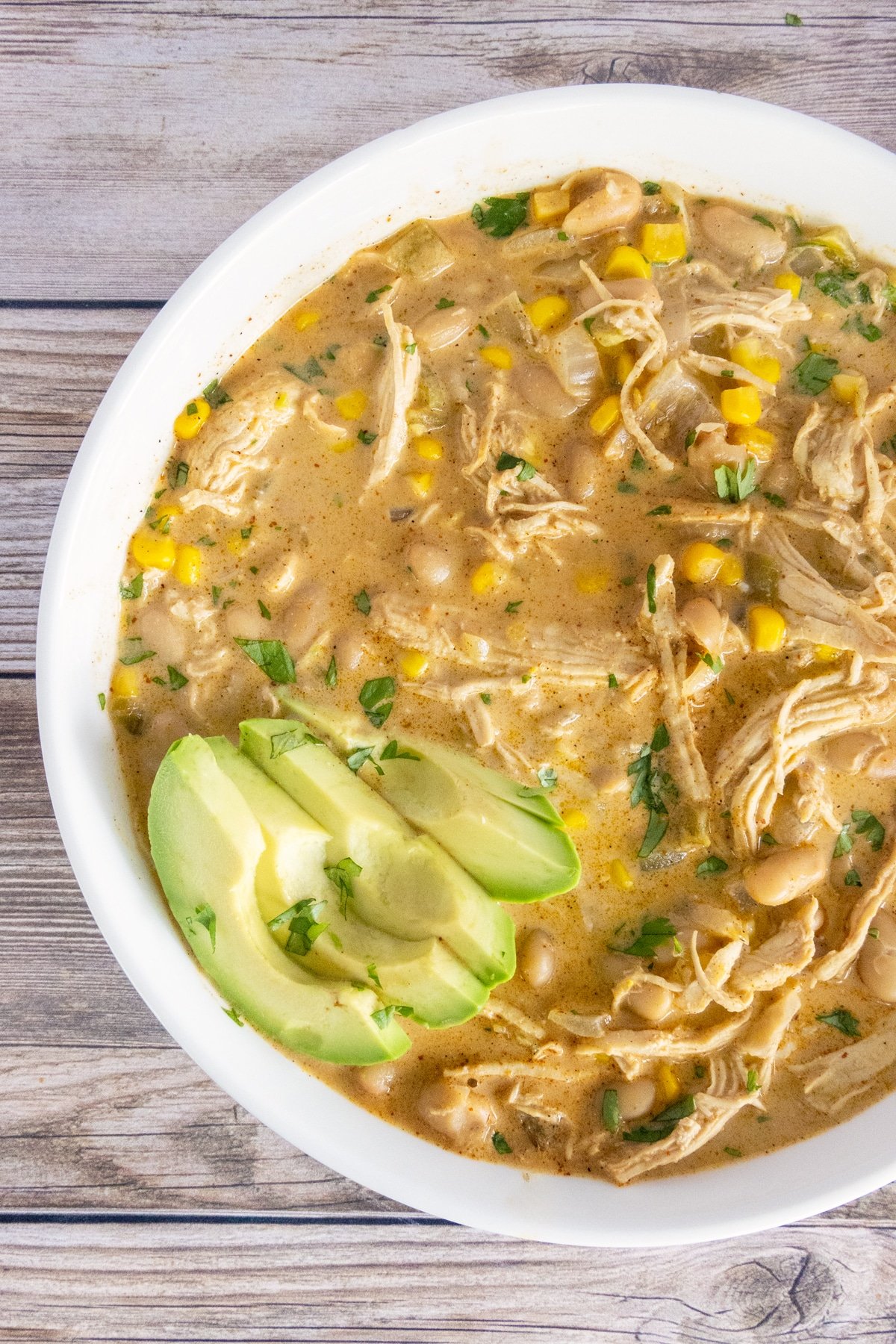 White chicken chili in a white bowl with avocado garnish. 